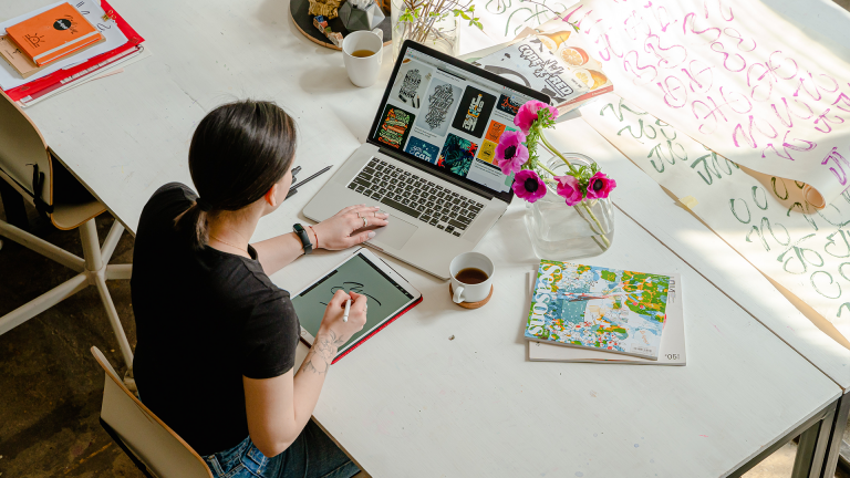 Woman writing on tablet in front of laptop